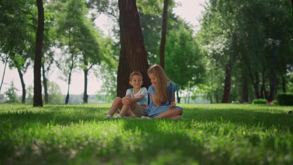 Smiling Siblings Play on Grass Under Tree