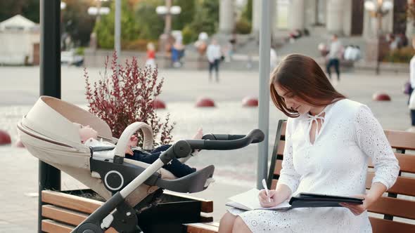 Mother Sitting on Banch with a Baby in Pram and Read Papers