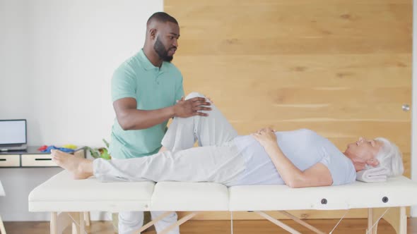 Video of african american male physiotherapist exercising with caucasian senior woman