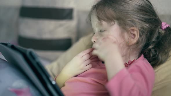 CU: Portrait of Pretty Little Girl, Child Who Lies on the Sofa Under Blanket and Plays on a Tablet