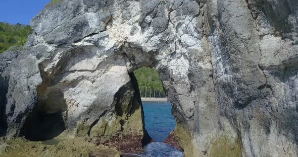 Aerial drone view flying through a natural rock arch the beach.