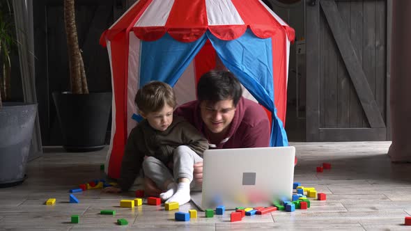 Father and son using laptop computer and lying in a small children's house