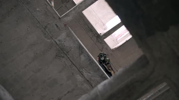 Stalker Man in Gas Mask Looks Down Through Floors of Old Ruined Abandoned Building