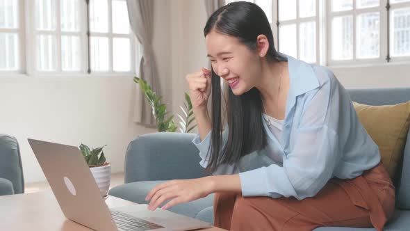 Asian Female Using Laptop And Celebrates In Living Room