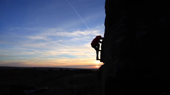 Silhouette of a man climbing boulders while bouldering.