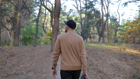 The guy in a black cap walks in the wood with a camera in his hand