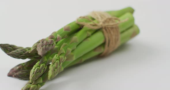 Video of close up of bundle of fresh asparagus over white background