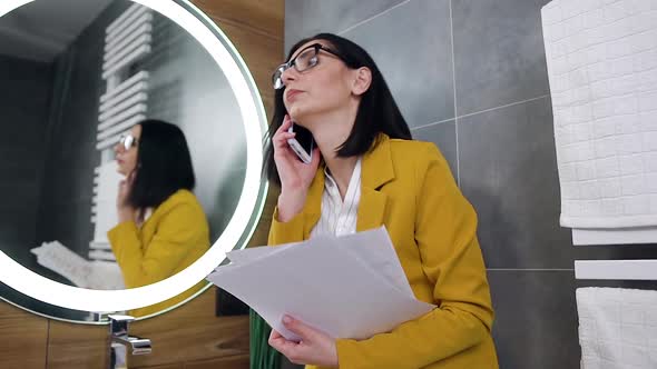 Stylish Young Brunette in Office Clothes Has Phone Conversation Near the Bathroom Mirror