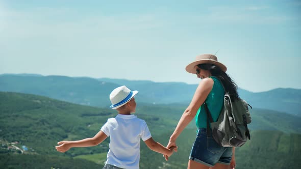 Joyful Tourist Mother and Son Clapping Hands Standing on Top of High Mountain