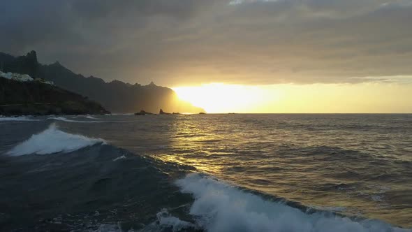 Flight Above Ocean Waves Facing Beautiful Sunset and Mountains on Horizon. Aerial Drone Shot of