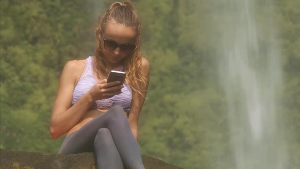 Nice Girl in Sunglasses Reads Sms Near Waterfall