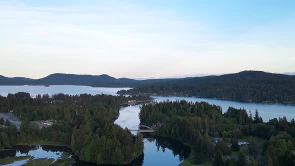 Backwardsing aerial shot over forests and Sooke river on Vancouver Island. Cameraement revealing bri