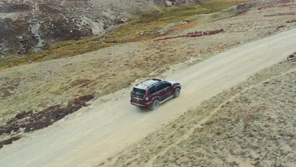 Aerial drone of a red suv driving along a dirt road path in the high-altitude alpine plain and mount