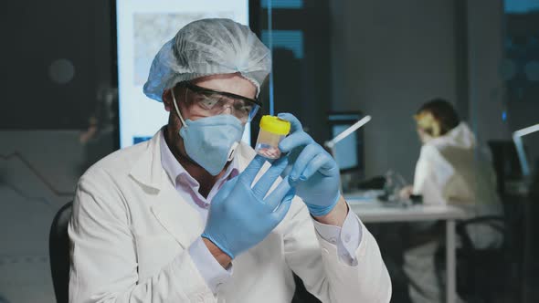 Male Scientist in Protective Gear and Gloves Examines Pills While Studying a New Cure