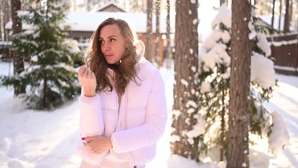 Winter Sunny Cold Portrait in Snowfall of Beautiful Young Woman in a White Warm Outwear Down Jacket