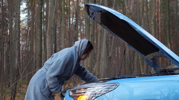 Woman Looks Under Hood of Broken Car Standing Forest Road