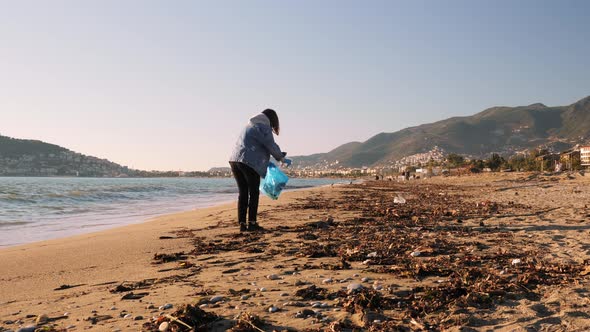 Volunteer picking up trash and collecting it in plastic bag while cleaning sea beach.