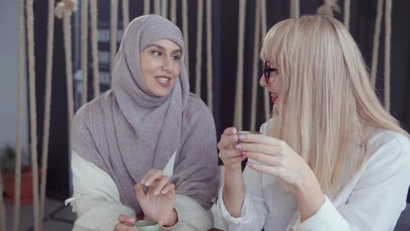 Arabian Woman Is Talking Secret To Her Blonde Female Friend During Drinking Tea