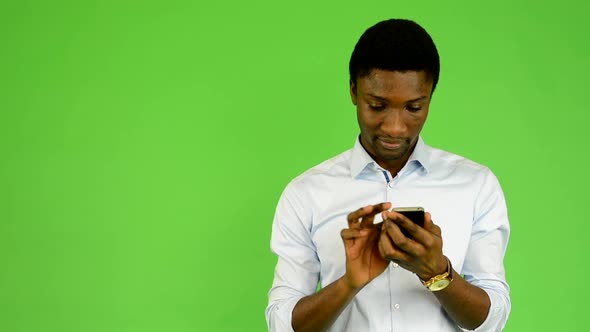 Young Handsome Black Man Works on Smartphone and Smiles - Green Screen - Studio