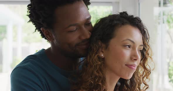 Profiles of happy biracial couple embracing, standing at window and looking into distance