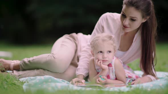 Young Mother And Daughter Reading Book Lying On Grass At Park