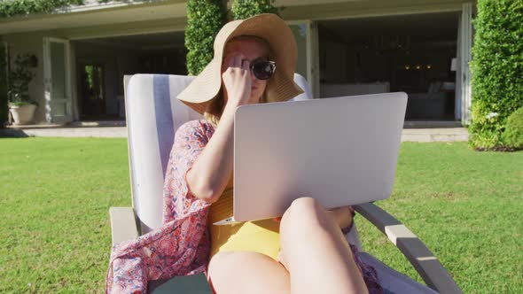 Caucasian woman using laptop while sunbathing on a deck chair in the garden