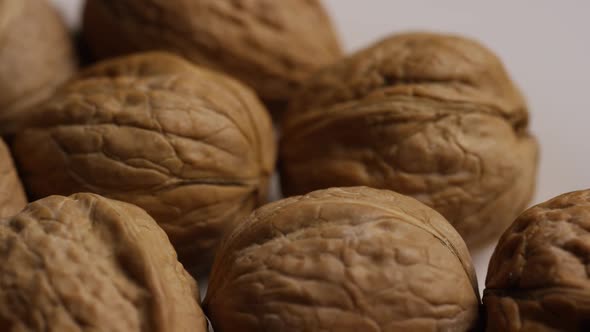 Cinematic, rotating shot of walnuts in their shells on a white surface 