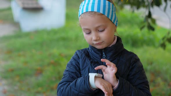 Child using smartwatch outdoor in autumn park Kid talking on vdeo call on the smartphone alt