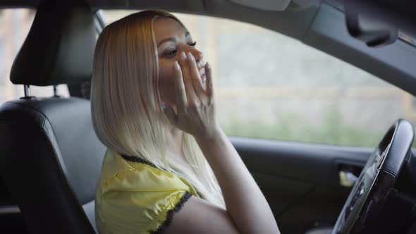 Positive Beautiful Caucasian Woman Checking Make-up and Winking Looking at Rear View Mirror. Side