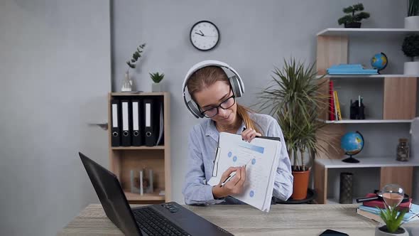 Woman in Headphones Holding in Hands Financial Report Talking at Webcam During Videocall