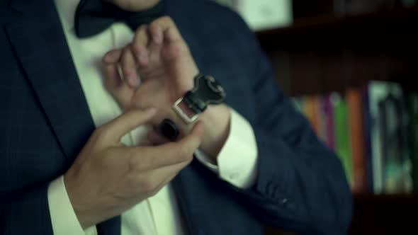 Morning  groom's preparations. Man puts on, fasten watch on wrist near bookshelves. Accessories