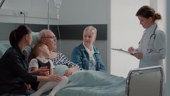 Doctor Doing Checkup Visit with Family Visiting Sick Pensioner in Hospital Ward