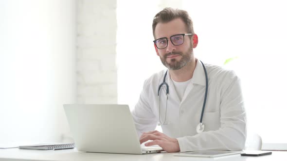 Doctor Smiling at Camera While Using Laptop in Office