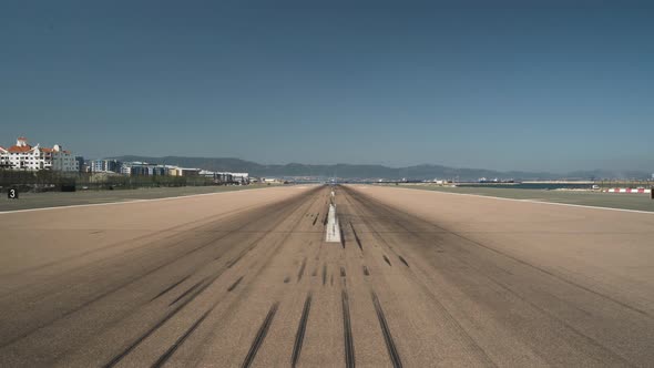 Empty runway with tire marks at Gibraltar airport, cloudless sky above.