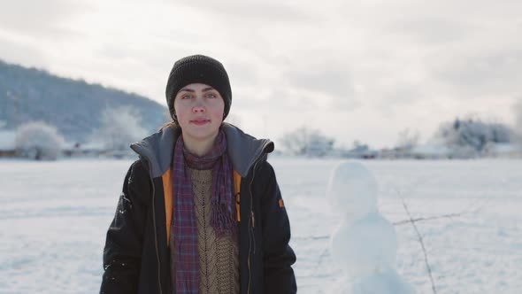 Portrait of a pretty caucasian smiling young woman in winter clothes and a hat in a snowy park.