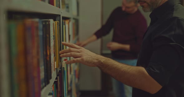 Closeup a Man Takes a Book From a Library Shelf a Selection of Interesting Literature