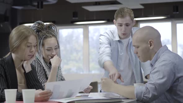 Four Young Caucasian Coworkers Discussing Paperwork in Office