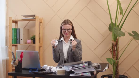 Woman office worker clutches paper in hands due to irritation and stress while sitting at table