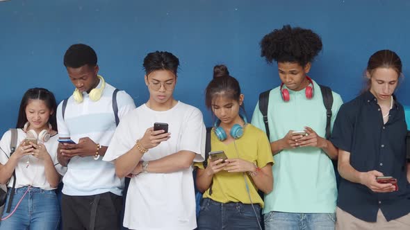 Group of Six Multiethnic Teenagers Chatting with the Smartphone on a Blue Wall