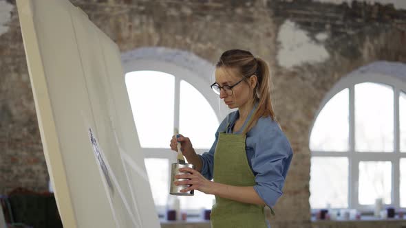 Female Artist Working with Large Paintbrush Standing in Front Wide Canvas