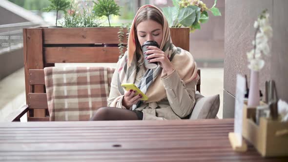 woman drinking coffee from a disposable cup on the street and texting on phone