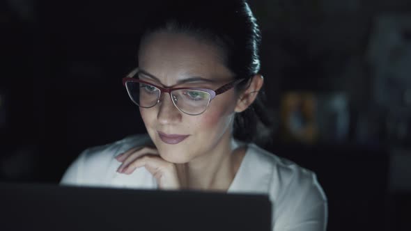 Woman in Glasses Works on a Laptop in the Dark. Portrait of a Girl Spending Time at the Computer