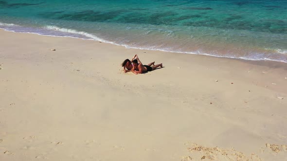 Teenage lovers tan on idyllic resort beach vacation by turquoise sea with bright sandy background of