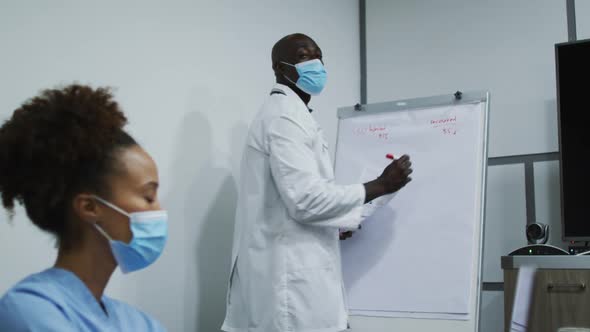 African american male doctor in face mask giving presentation to mixed race female doctor in office