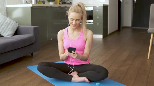 Cute Woman Sitting on Yoga Mat and Browsing Mobile Phone for Songs