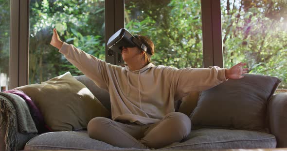 Asian girl smiling and gesturing while wearing vr headset sitting on the couch at home