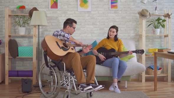 Young Disabled Man in a Wheelchair Guitarist Teaches a Girl To Play Guitar