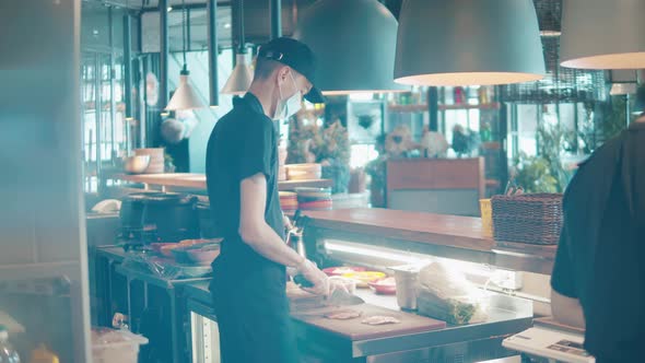 Male Cook in a Face Mask is Cutting Pieces of Meat