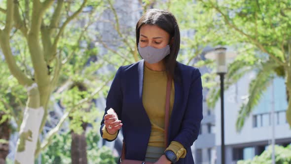 African american woman wearing face mask disinfecting hands in the street