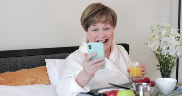 Cheerful Old Lady Looking at Her Modern Smartphone Screen and Laughing. Elderly Woman in Good Mood